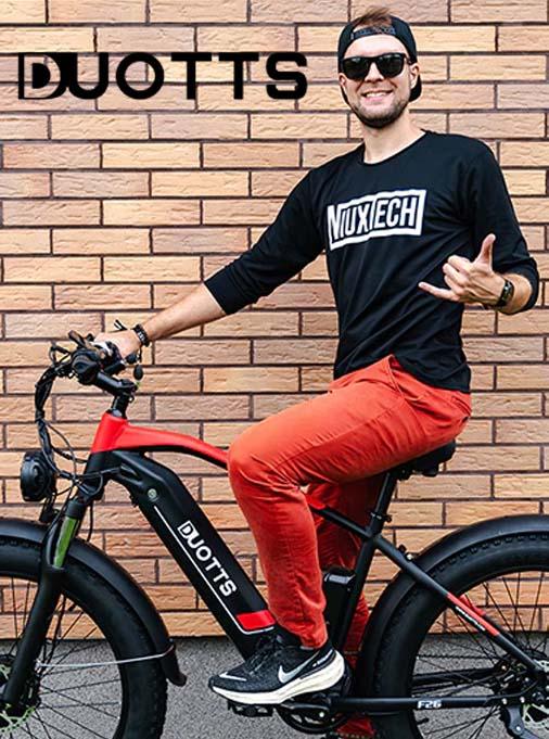 Duotts electric bike side view with rider, black and red frame, urban brick wall background