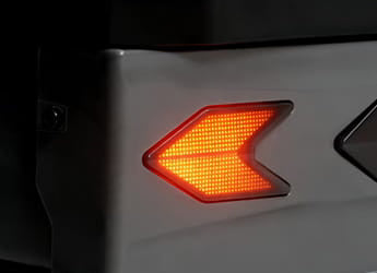 Close-up of a vehicle rear light assembly with a glowing amber left turn signal on a dark and light-colored body panel.