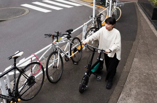 Woman walking a black electric bike beside parked bicycles on a city sidewalk