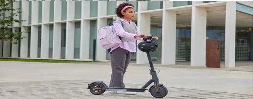 Person riding a black electric scooter on city pavement, side view