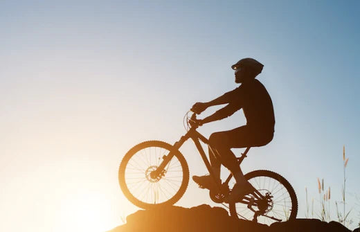 Electric mountain bike side view with rider cycling uphill at sunset outdoors