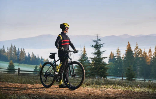 Electric mountain bike side view outdoors with rider on a trail in wooded landscape