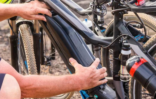 Person removing black electric bike battery from frame, close-up of component outdoors