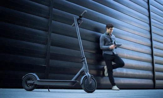 Black electric scooter side view with person using tablet against modern wall