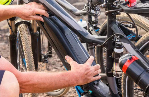Close-up of hands installing electric bike battery on black e-bike frame outdoors
