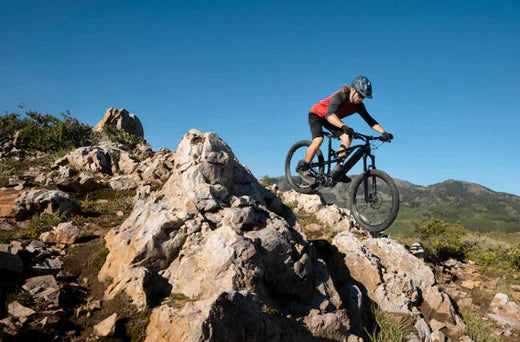 Electric mountain bike on rocky trail with rider wearing helmet, outdoor side view
