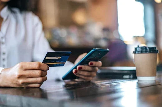 Person holding credit card and smartphone at a wooden table for online payment