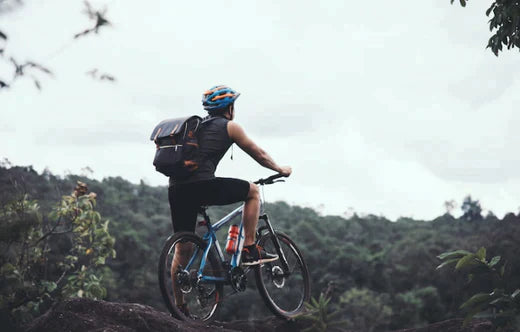electric bike in outdoor mountain setting, rider wearing helmet and backpack, side view