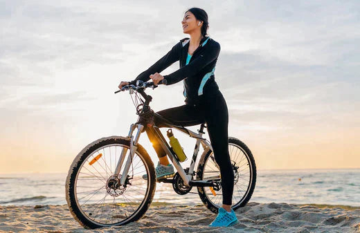 Woman with silver electric bike standing on beach at sunset, side view