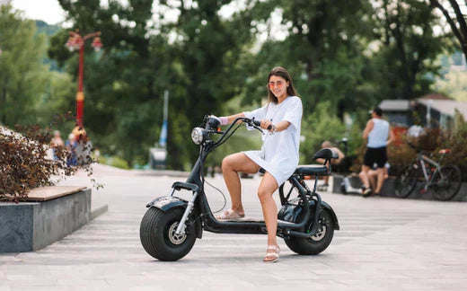 Woman riding black electric bike on city path, side view, green trees in background