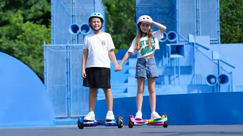 Two children holding hands on hoverboards in front of a blue futuristic structure.
